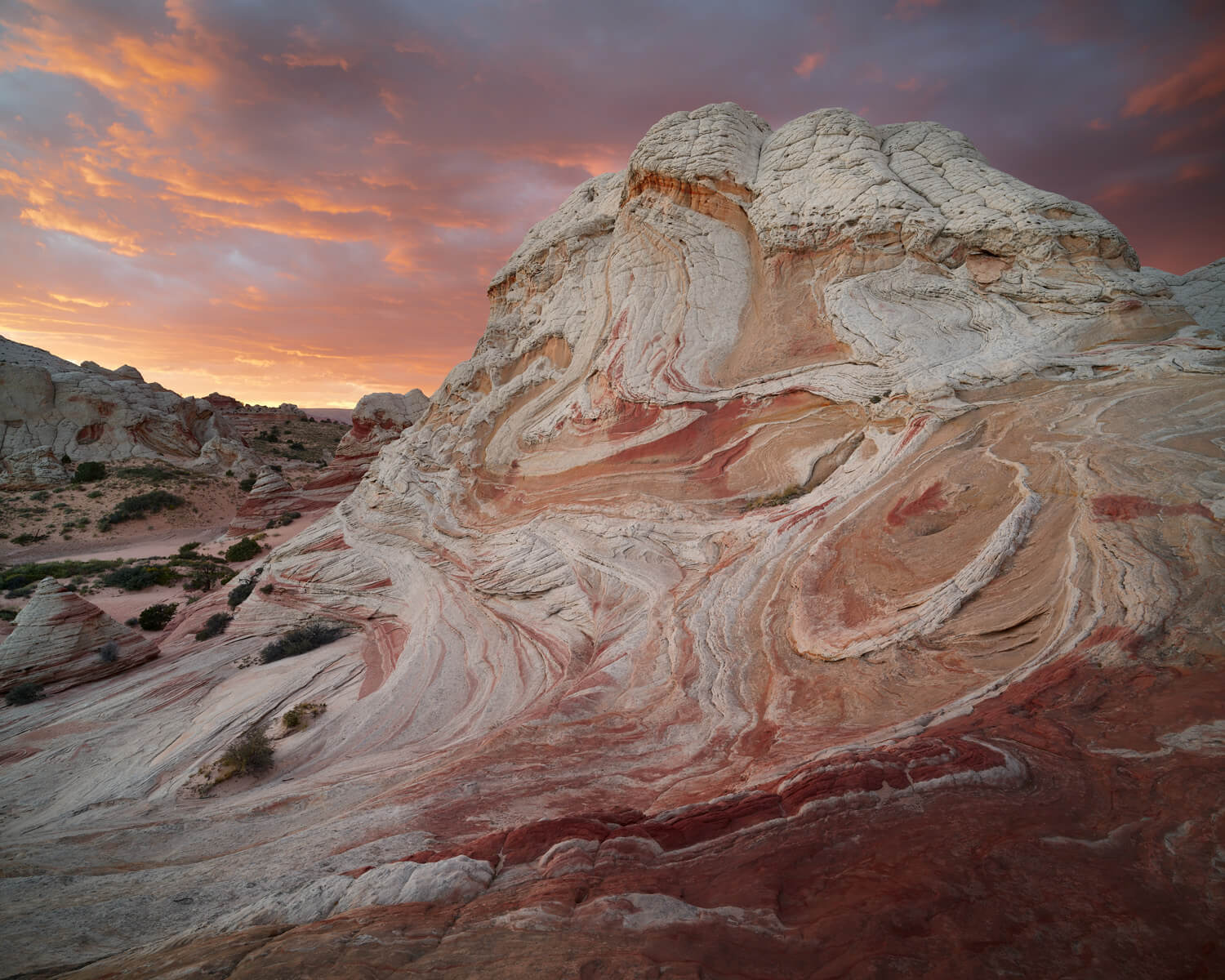 A striking geological formation with swirling red and white rock patterns in White Pocket, Arizona, captured at sunset with a vibrant sky in the background.