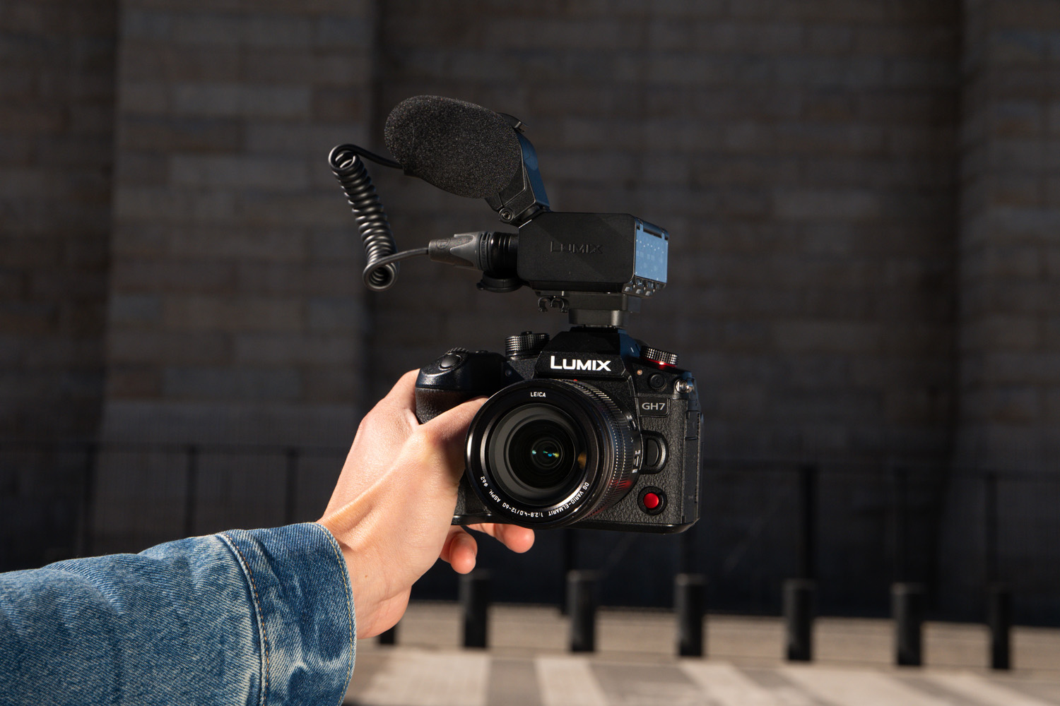 Close up of Panasonic Lumix GH7 camera with microphone attached being held as if taking a selfie in a street scene