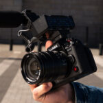 Close up of Panasonic Lumix GH7 camera with microphone attached being held in a street scene