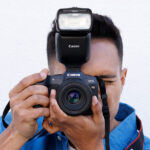 photo of man holding camera to his eye with Canon Speedlight EL-10 attached