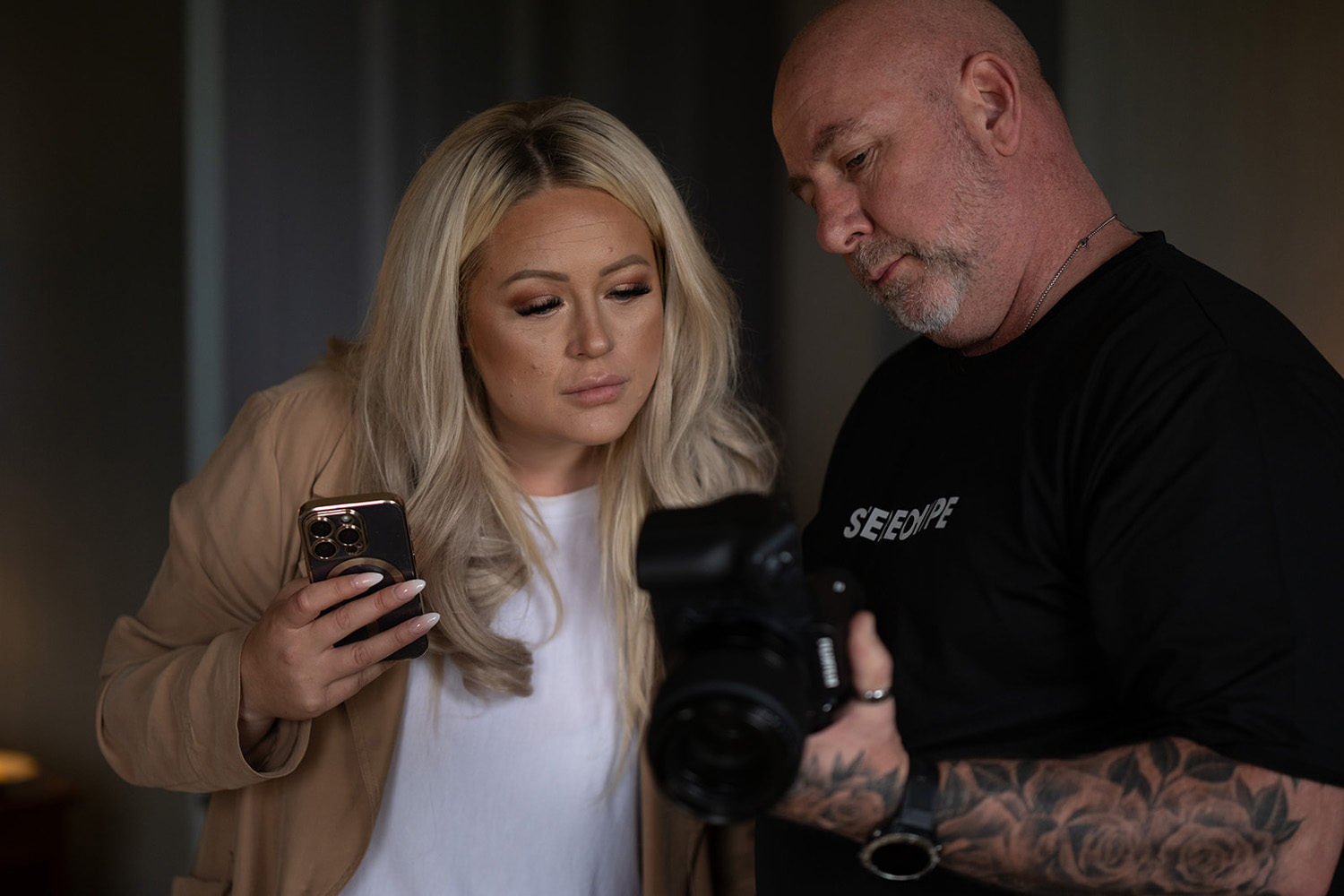 A female photographer with blonde hair is reviewing images on a camera with a male photographer. Both appear focused and are discussing the shots displayed on the camera screen.