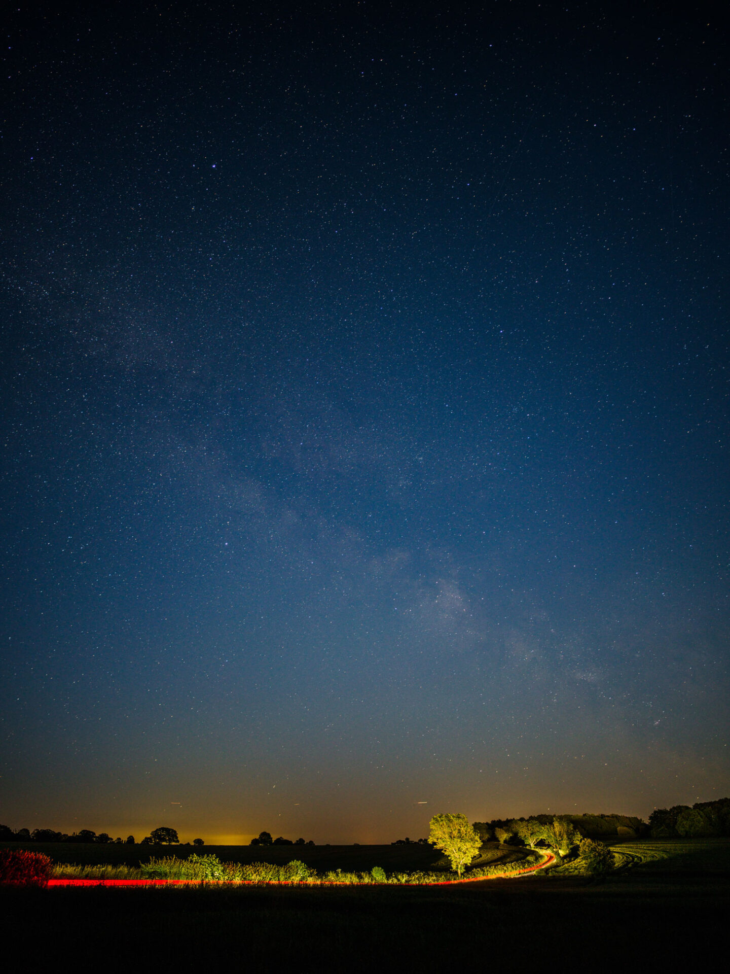 Night image of country lane with light trails from car moving around the curve of a bend between fields